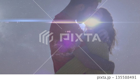 Hugging couple sharing sunset at hilltop, wearing red shirt and knit sweater with sun flare 135588491