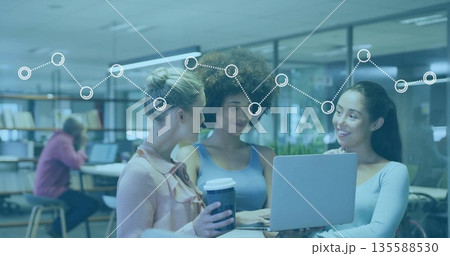 Collaborating women pointing at laptop holding coffee cups in modern workspace at high table Collaborating women pointing at laptop holding coffee cups in modern workspace at high table 135588530