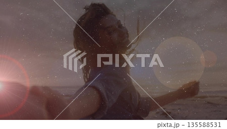 Spinning woman holding smartphone on sunset beach in long sleeves, with lens flare, grain overlay Spinning woman holding smartphone on sunset beach in long sleeves, with lens flare, grain overlay 135588531