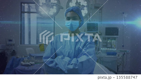 Standing female surgeon crossing arms under surgical lights in operating room, with monitors trays Standing female surgeon crossing arms under surgical lights in operating room, with monitors trays 135588747