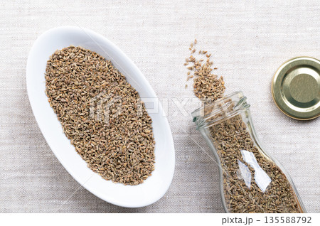 Aniseed, anise seeds, in white bowl on linen. Anise fruits, mistakenly called seeds, from the plant Pimpinella anisum, used to flavor food, candy, and alcoholic drinks, around the Mediterranean. Photo Aniseed, anise seeds, in white bowl on linen. Anise fruits, mistakenly called seeds, from the plant Pimpinella anisum, used to flavor food, candy, and alcoholic drinks, around the Mediterranean. Photo 135588792