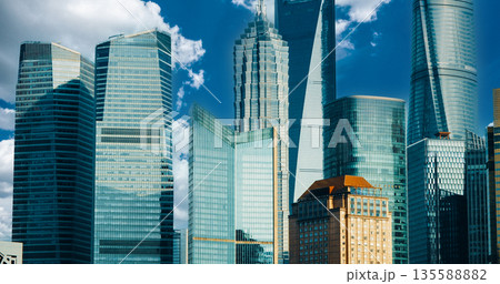 Modern glass skyscrapers with historic golden building during daytime under bright blue sky with white clouds, showing contrast between contemporary and heritage architecture Modern glass skyscrapers with historic golden building during daytime under bright blue sky with white clouds, showing contrast between contemporary and heritage architecture 135588882