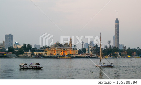 Evening view of the Nile River in Cairo. Two feluccas sail on the water. The background features city buildings and the Cairo Tower. Evening view of the Nile River in Cairo. Two feluccas sail on the water. The background features city buildings and the Cairo Tower. 135589594