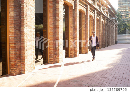 Young man walking through brick corridor in sunlight Young man walking through brick corridor in sunlight 135589796