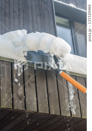 Clearing heavy snow from a house roof with a shovel. 135589966