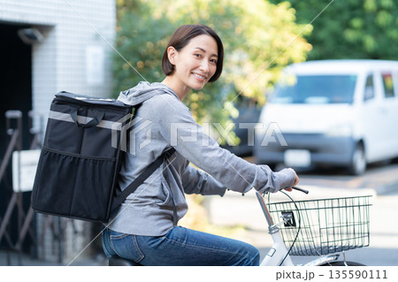 自転車でフードデリバリーをする配達員の女性 自転車でフードデリバリーをする配達員の女性 135590111