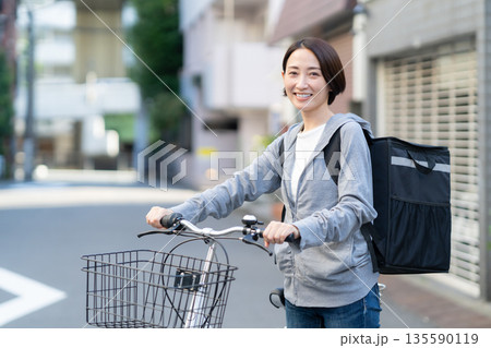 自転車でフードデリバリーをする配達員の女性 自転車でフードデリバリーをする配達員の女性 135590119