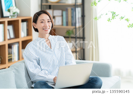 リビングのソファに座ってパソコンを見るミドルの女性 リビングのソファに座ってパソコンを見るミドルの女性 135590145