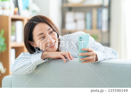 リビングのソファで寝転んでスマホを見るミドルの女性 リビングのソファで寝転んでスマホを見るミドルの女性 135590149
