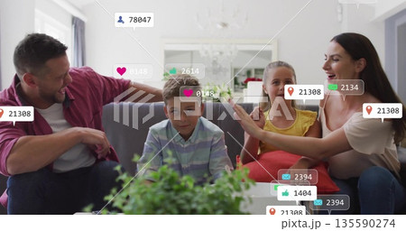 Sitting family on grey sofa in bright living room, being surrounded by floating notification icons Sitting family on grey sofa in bright living room, being surrounded by floating notification icons 135590274