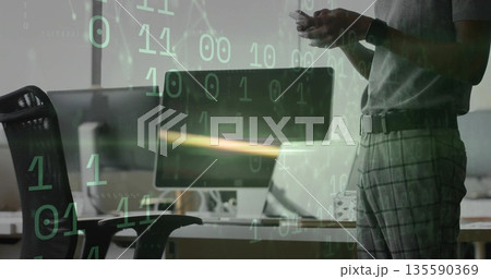 Standing developer holding smartphone in office near desk with monitor, binary overlay, copy space Standing developer holding smartphone in office near desk with monitor, binary overlay, copy space 135590369