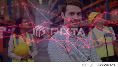 Supervising manager guiding team in warehouse aisle, with vests, shelves, boxes, network overlay 135590424