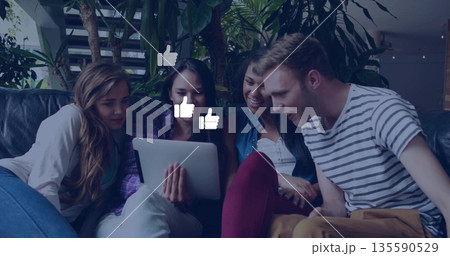 Leaning friends viewing tablet on leather couch in lounge with plants, floating thumbs-up graphics Leaning friends viewing tablet on leather couch in lounge with plants, floating thumbs-up graphics 135590529