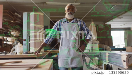 Standing African American carpenter in apron at workshop bench, with lumber, dust extraction hose 135590629