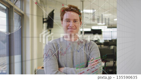 Standing analyst in gray sweater behind transparent panel in modern office, with financial charts 135590635