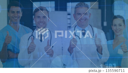 Smiling team wearing lab coats scrubs giving thumbs-up in hospital corridor, stethoscopes ID badges 135590711