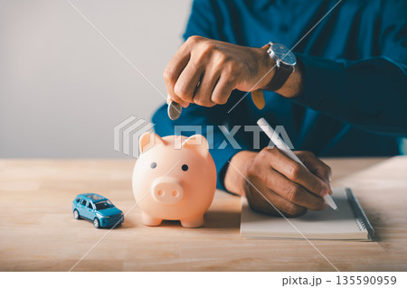 Man saves money in piggy bank for first car buying, writing notes to calculate saving cost, insurance and tax, planning budget for purchase using bank loan and personal savings Man saves money in piggy bank for first car buying, writing notes to calculate saving cost, insurance and tax, planning budget for purchase using bank loan and personal savings 135590959