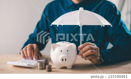 man holds white umbrella over piggy bank to protect money, financial insurance concept covers risk, umbrella finance collage shows savings security on wooden desk using calculator man holds white umbrella over piggy bank to protect money, financial insurance concept covers risk, umbrella finance collage shows savings security on wooden desk using calculator 135590981