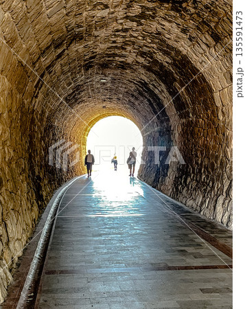 three individuals traverse shadowed pathway, people moving towards glowing tunnel entrance 135591473