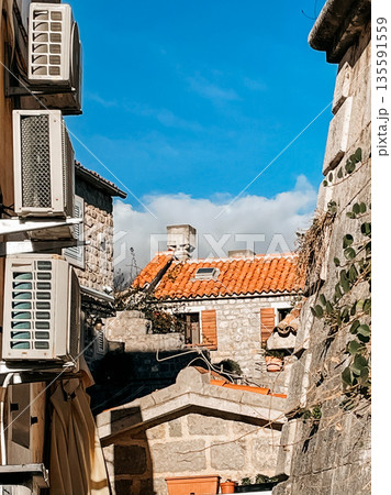 terracotta tiled rooftop with chimneys and ducts, city skyline behind sunlit building with vents and cables 135591559