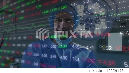 Surgeon wearing blue scrubs posing in OR, showing financial overlay, light and control panel 135591954