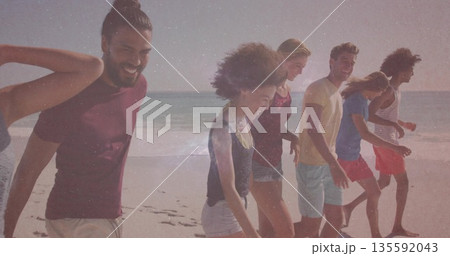 Group of six friends walking barefoot along ocean edge amid gentle waves, wearing summer attire 135592043