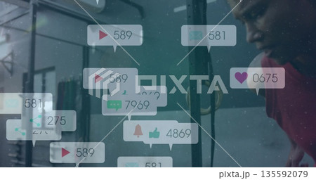 Exercising man in red shirt leaning on pullup rig at gym, with floating notifications, copy space 135592079