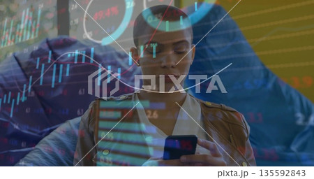 Analyzing woman wearing brown leather jacket checking smartphone on home sofa with financial charts 135592843