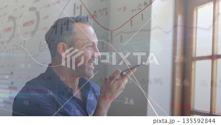 Mature man in blue shirt dictating on smartphone in office by wooden window, with financial charts Mature man in blue shirt dictating on smartphone in office by wooden window, with financial charts 135592844
