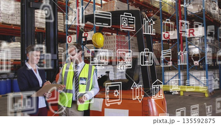 Reviewing warehouse staff checking stock on clipboard beside orange forklift, digital overlay icons 135592875