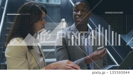 Reviewing colleagues in corporate attire analyzing overlay charts on office stairwell, with laptop 135593044