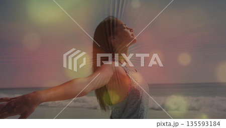 Stretching arms and tilting head, woman wearing sleeveless top on sandy beach at sunrise, warm glow Stretching arms and tilting head, woman wearing sleeveless top on sandy beach at sunrise, warm glow 135593184