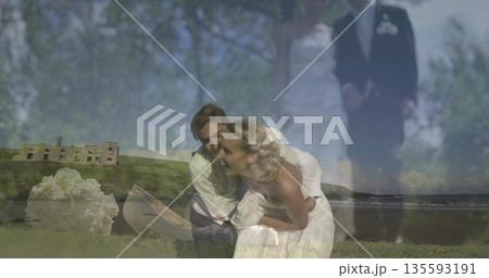 Kneeling bride in white dress hugging with groom in suit on grassy shoreline, with bouquet, shoes 135593191