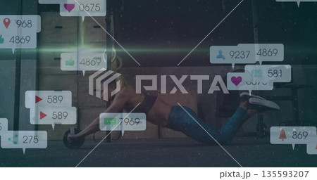 Kneeling woman wearing sportswear rolling ab roller on mat at gym, floating social media icons Kneeling woman wearing sportswear rolling ab roller on mat at gym, floating social media icons 135593207