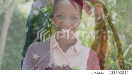 Smiling woman in pink shirt holding bowl of greens in garden with translucent American flag overlay 135593213