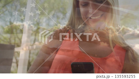 Holding woman wearing coral top smiling at smartphone on backyard porch deck, with flag overlay Holding woman wearing coral top smiling at smartphone on backyard porch deck, with flag overlay 135593255