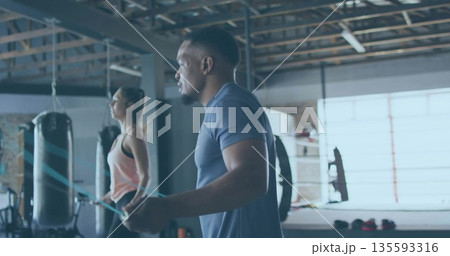 Skipping man wearing navy T-shirt and shorts holding jump rope in boxing gym, with punching bags Skipping man wearing navy T-shirt and shorts holding jump rope in boxing gym, with punching bags 135593316