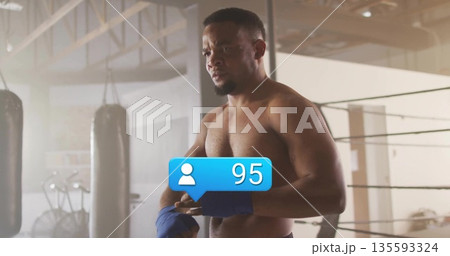 Wrapping hands shirtless boxer in gym with ring ropes, blue wraps, 95 follower icon and equipment 135593324