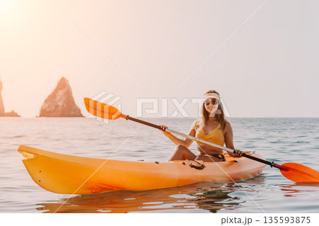 Kayaking Woman Ocean Paddle - A woman in a yellow bikini kayaks on a calm ocean with two rocky islands in the background. Kayaking Woman Ocean Paddle - A woman in a yellow bikini kayaks on a calm ocean with two rocky islands in the background. 135593875