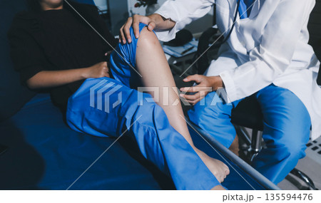 Asian male doctor examining foot of female patient sitting on bed in hospital room. Performing medical checkup. Diagnosing injury. Providing healthcare. Podiatry. Physical therapy. And rehabilitation Asian male doctor examining foot of female patient sitting on bed in hospital room. Performing medical checkup. Diagnosing injury. Providing healthcare. Podiatry. Physical therapy. And rehabilitation 135594476