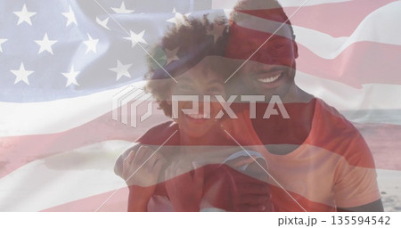 Hugging couple standing on sandy shoreline, under translucent American flag overlay 135594542
