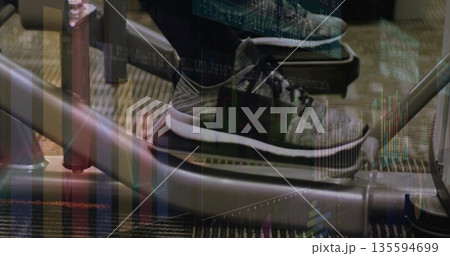 Pressing sneaker-clad foot down on elliptical pedal at gym with financial chart overlays Pressing sneaker-clad foot down on elliptical pedal at gym with financial chart overlays 135594699