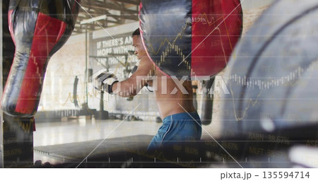 Punching shirtless boxer practicing bag work at gym, with punching bags and financial chart overlay 135594714