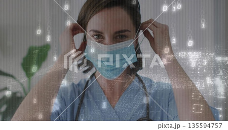 Clinician adjusting surgical mask in clinic, wearing blue scrubs, stethoscope, binary code overlay Clinician adjusting surgical mask in clinic, wearing blue scrubs, stethoscope, binary code overlay 135594757