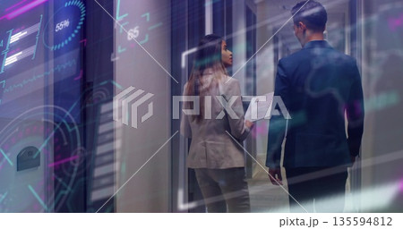 Suited professionals walking through office hallway, viewing holographic charts with printed report Suited professionals walking through office hallway, viewing holographic charts with printed report 135594812