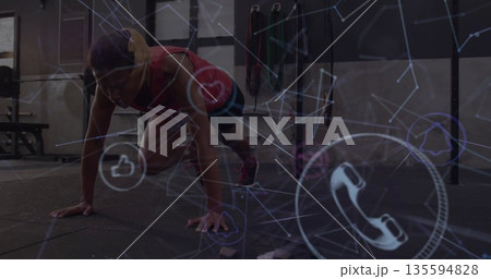 Mid-adult female wearing sportswear performing mountain climber exercise in gym, with digital icons Mid-adult female wearing sportswear performing mountain climber exercise in gym, with digital icons 135594828