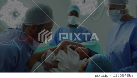 Handing newborn wrapped in blanket by father in hospital to mother, with operating table, lights Handing newborn wrapped in blanket by father in hospital to mother, with operating table, lights 135594868