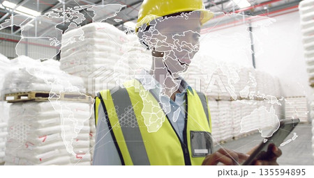 Worker wearing safety gear reviewing inventory on tablet in warehouse, with bulk bags, map overlay Worker wearing safety gear reviewing inventory on tablet in warehouse, with bulk bags, map overlay 135594895