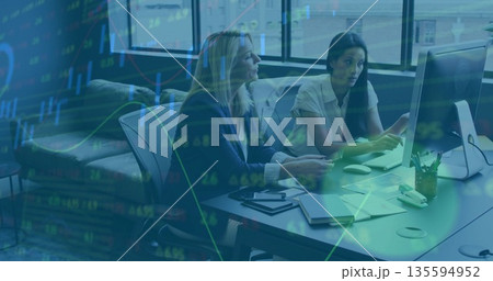 Collaborating experienced women reviewing reports at office desk, with financial data overlay 135594952