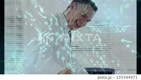 Smiling professional leaning over desk working on laptop in office, with circuit-pattern overlay Smiling professional leaning over desk working on laptop in office, with circuit-pattern overlay 135594971